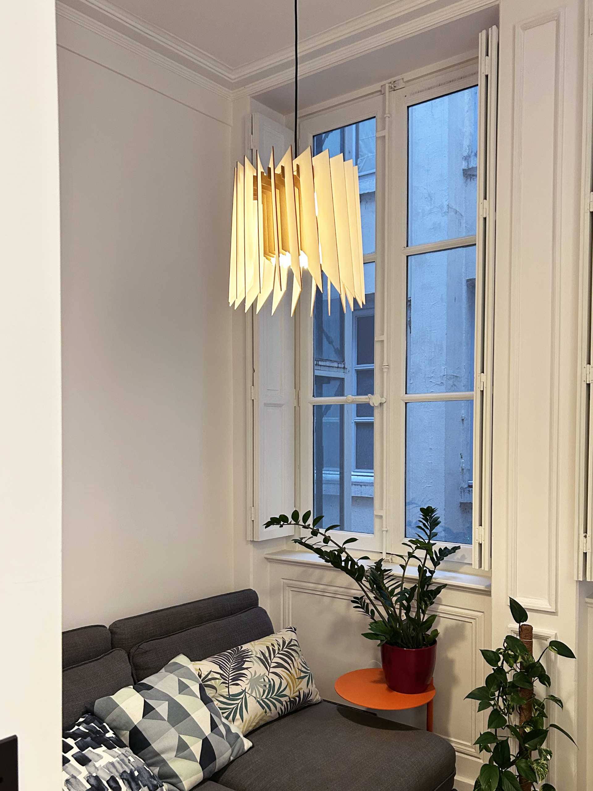 Une suspension en bois design au dessus d'un canapé et de plantes