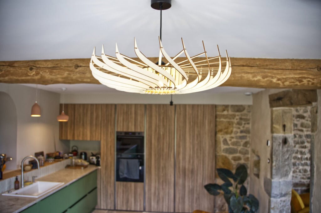 Suspension en bois Claudine la turbine dans un séjour avec poutre et mur en pierre