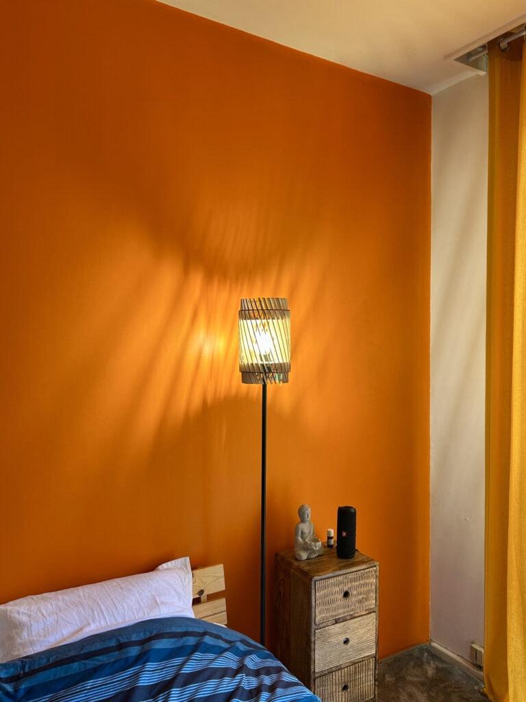 Lampadaire bois Alice dans une chambre au mur orange, près du lit