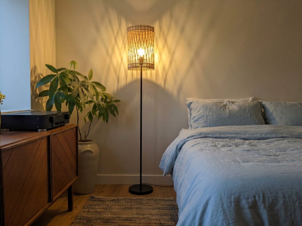 Lampadaire en bois Vincent près d'une plante et d'une banquette, mur clair