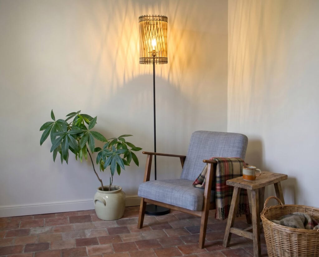 Lampadaire bois Vincent dans un salon, près d'un fauteuil et d'une plante verte