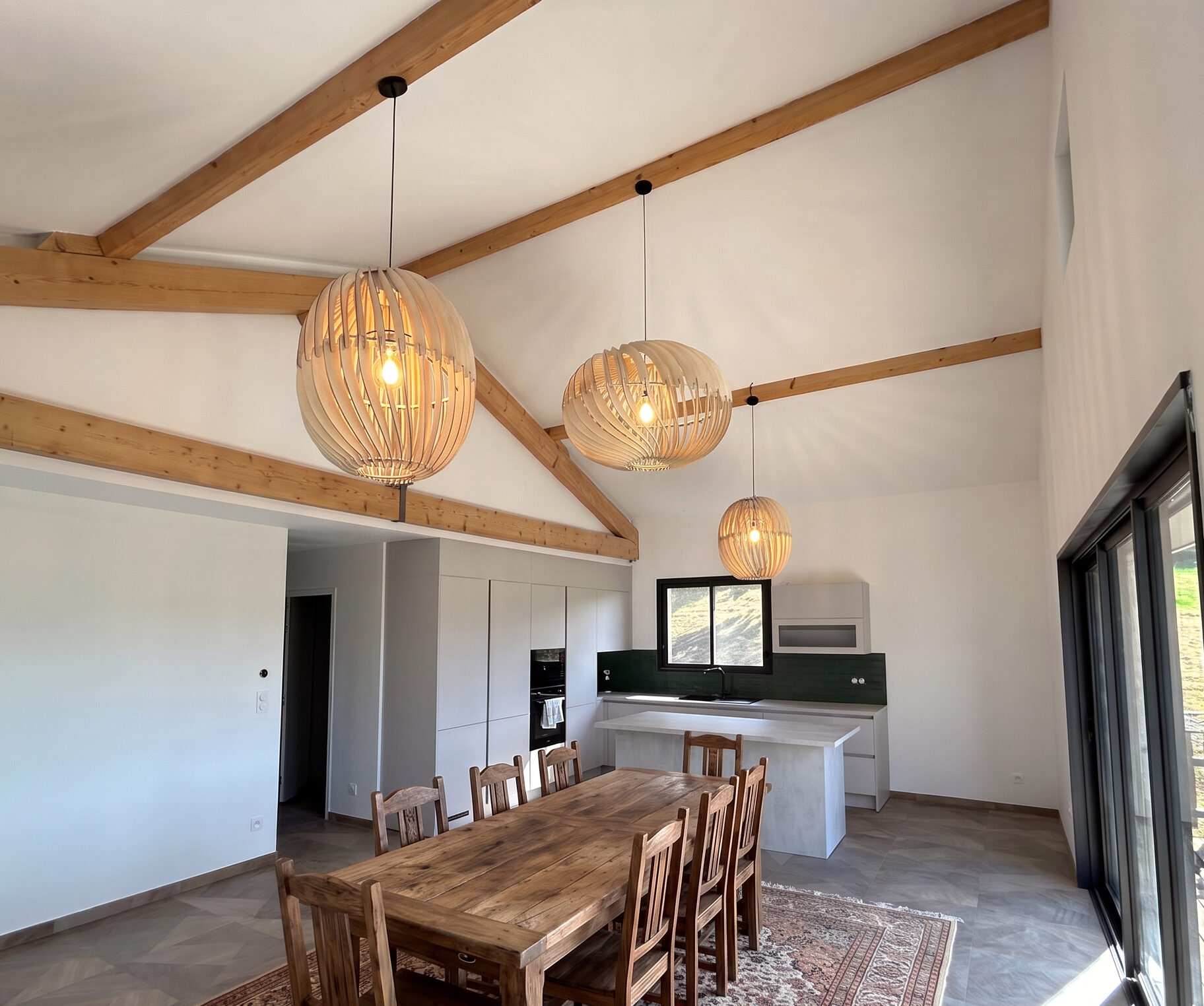 Salle à manger éclairée par trois suspensions en peuplier au-dessus d'une grande table en bois massif