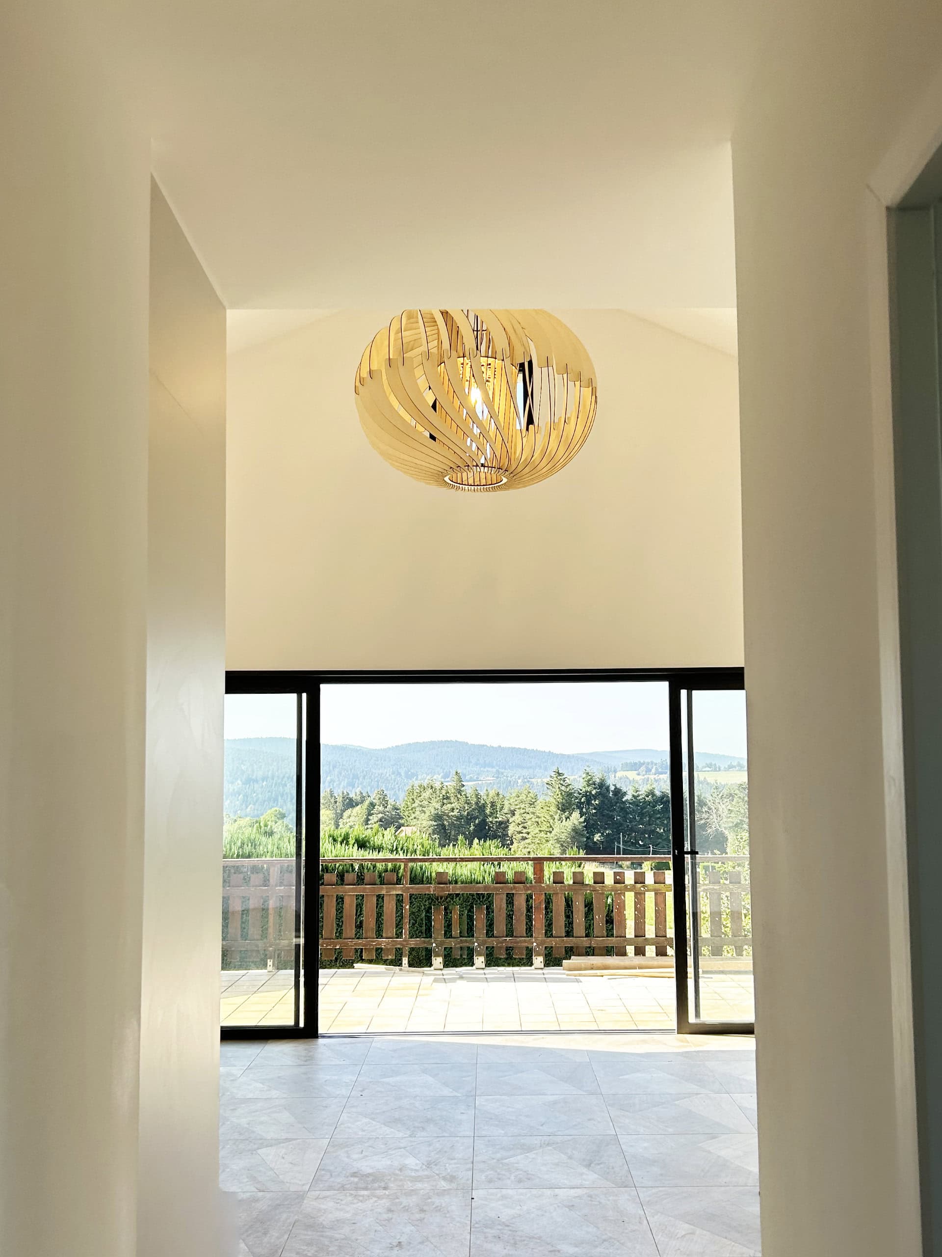Suspension en bois sur mesure aperçue depuis l'entrée du salon, terrasse et collines du Pilat en arrière-plan